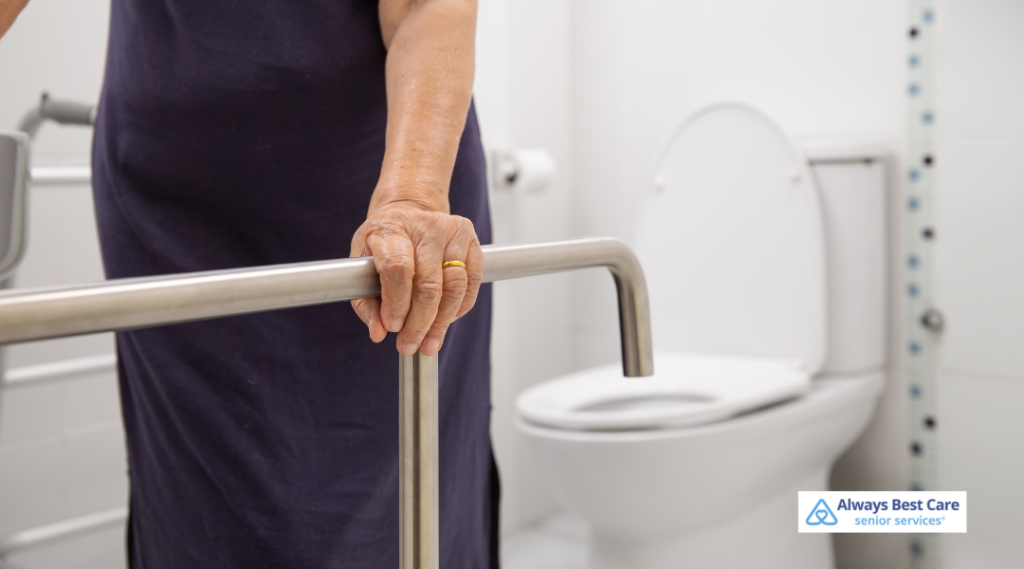 A close-up of a senior woman's hand holding a bathroom safety rail next to a toilet, emphasizing mobility assistance.