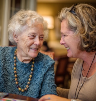 CARING COMPANION ASSISTING AN ELDERLY WOMAN DURING A WARM, ENGAGING MOMENT AT HOME, REFLECTING COMPASSIONATE HOME CARE SERVICES IN VERONA, WI THAT PRIORITIZE COMFORT AND FAMILY SUPPORT.