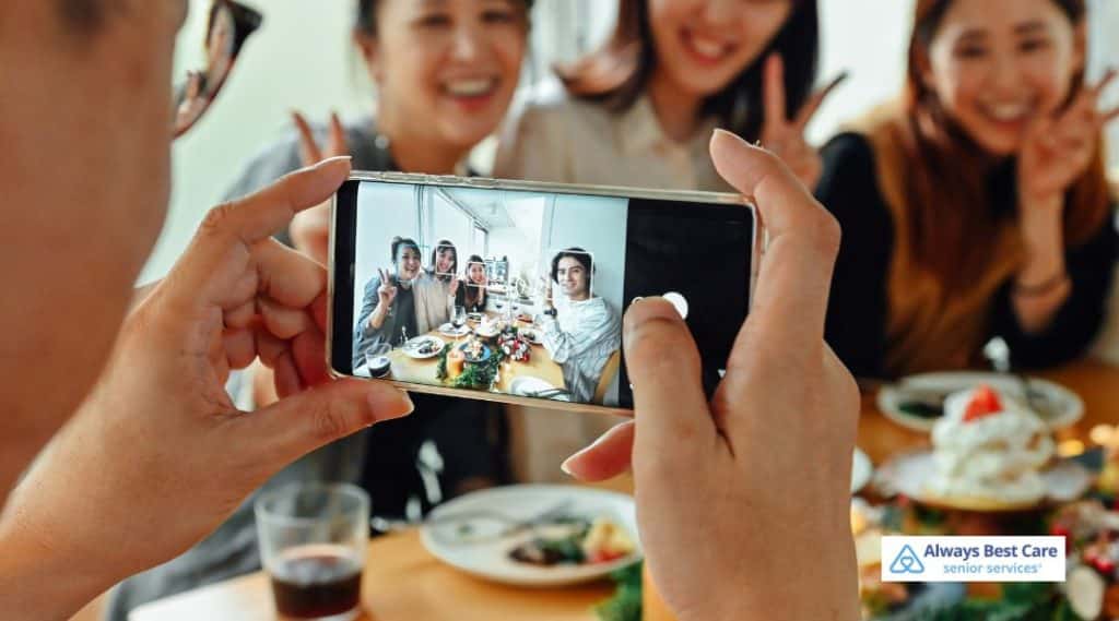 Person taking a photo on a smartphone of friends or family gathered around a shared meal, capturing joyful connection and meaningful moments across generations.