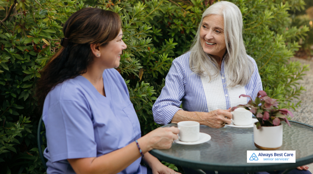 Caregiver and senior woman sharing tea and conversation outdoors, highlighting companionship and emotional support at home.