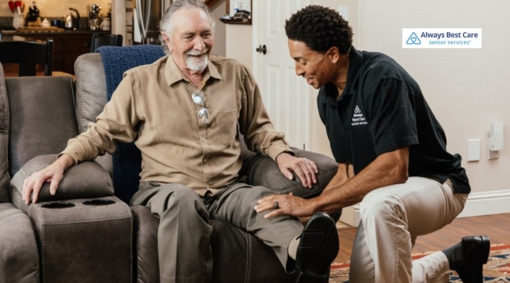 CAREGIVER SUPPORTING SENIOR MAN AS HE SETTLES INTO A RECLINER CHAIR