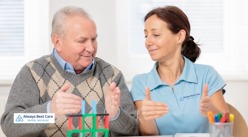 SENIOR MAN WORKING ON A COGNITIVE ACTIVITY GAME WITH AN ALWAYS BEST CARE CAREGIVER AT THE TABLE.