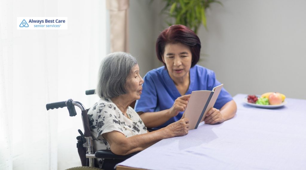 Caregiver reading aloud with a senior woman in a wheelchair, highlighting companionship and memory stimulation during home-based dementia care.