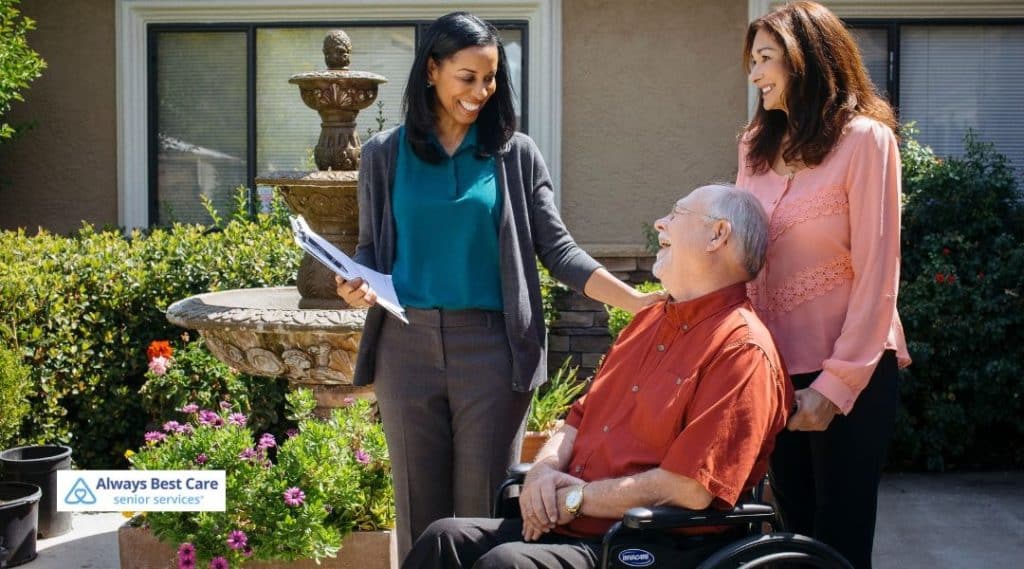 Care coordinator speaking with a senior using a wheelchair and a family member in a landscaped outdoor setting, reviewing care plans together.