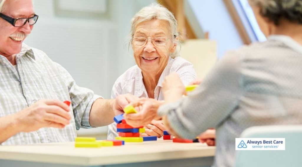 Group of seniors sitting at a table, smiling and stacking colorful blocks during a cognitive activity session.