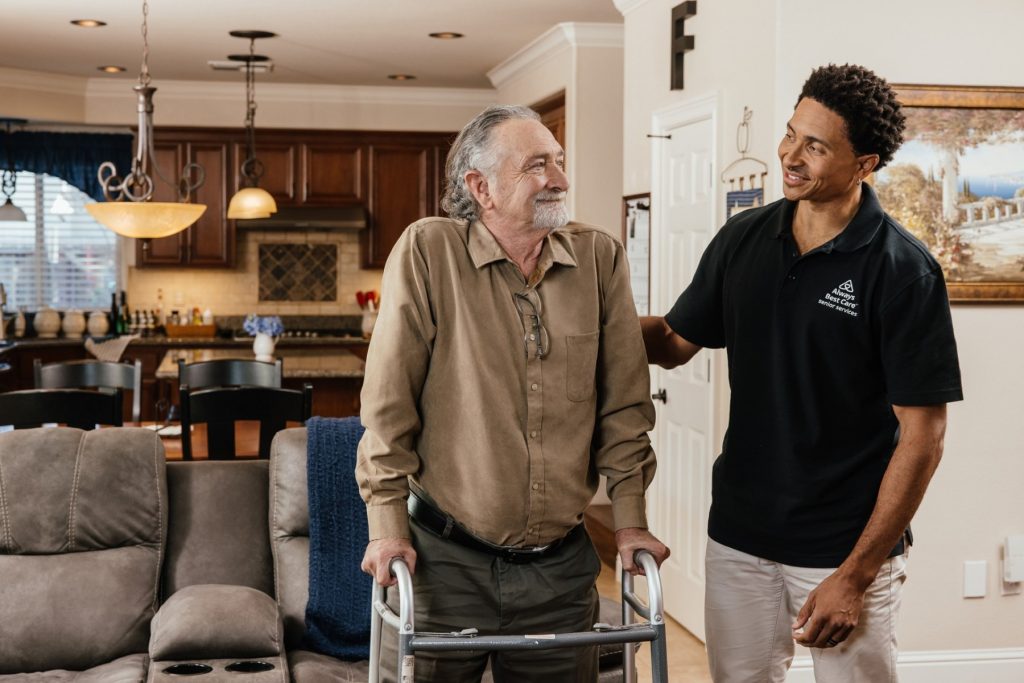 Caregiver supporting senior man using a walker in his living room