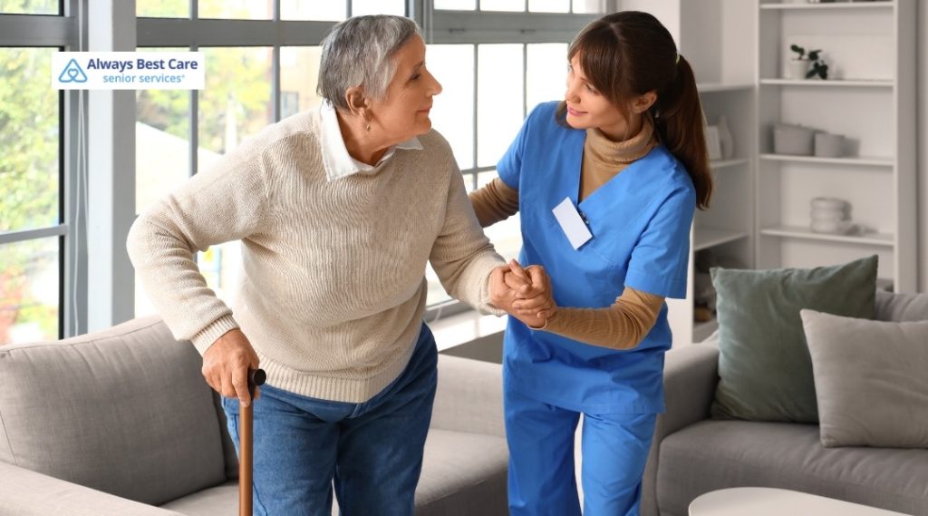 Caregiver helping a senior woman stand safely in a living room