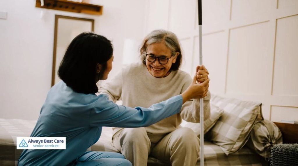 SPINA BIFIDA HOME CARE IN ORLANDO: PERSONALIZED SUPPORT FOR DAILY LIVING AND INDEPENDENCE 6 CAREGIVER SUPPORTING AN OLDER WOMAN WITH A MOBILITY AID BESIDE HER BED.