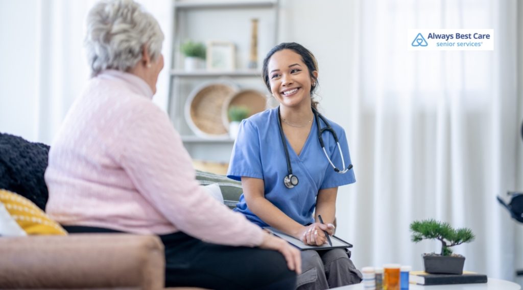 A caregiver sitting with a senior woman, both engaged in conversation, with a friendly and caring atmosphere in a well-lit living room.