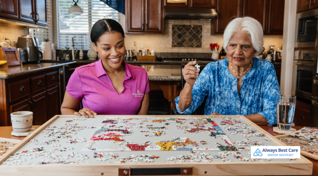 Senior woman and Always Best Care caregiver sitting at a kitchen table completing a large jigsaw puzzle as a stimulating activity for early dementia