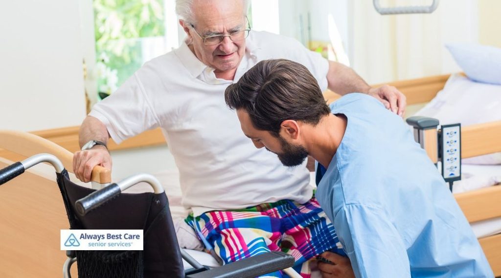 Caregiver assisting an older man with a safe transfer from bed to wheelchair.