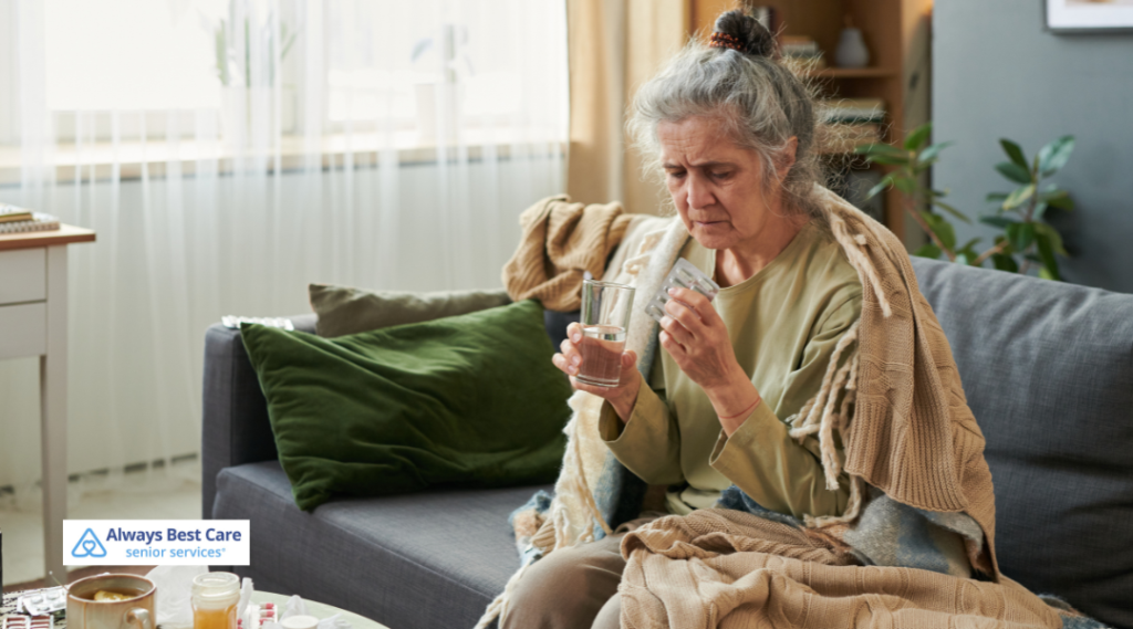 Senior woman wrapped in a blanket on a couch, holding a glass of water and examining her medication.