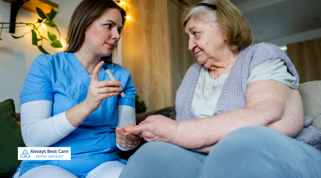 Always Best Care caregiver showing a lancet pen to an elderly woman while explaining blood sugar monitoring at home.