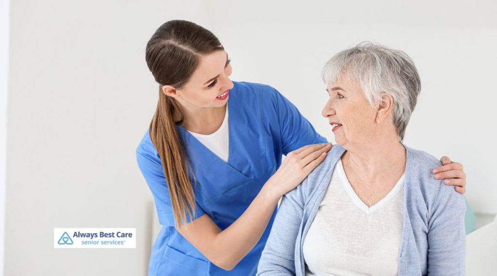 Caregiver placing a comforting hand on an older woman’s shoulder, sharing a calm and supportive moment indoors.