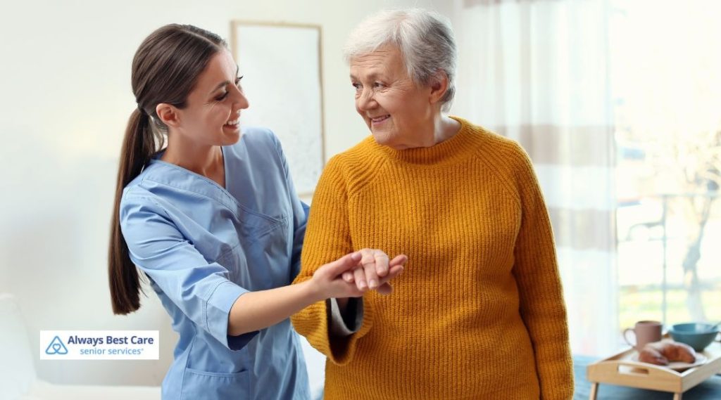 Caregiver gently assisting an older woman as they walk together indoors, offering support and reassurance.