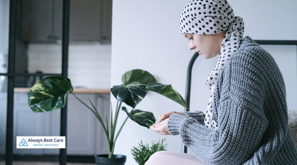 oman wearing a polka-dot headscarf and gray cardigan sitting at home, looking down at her hands.
