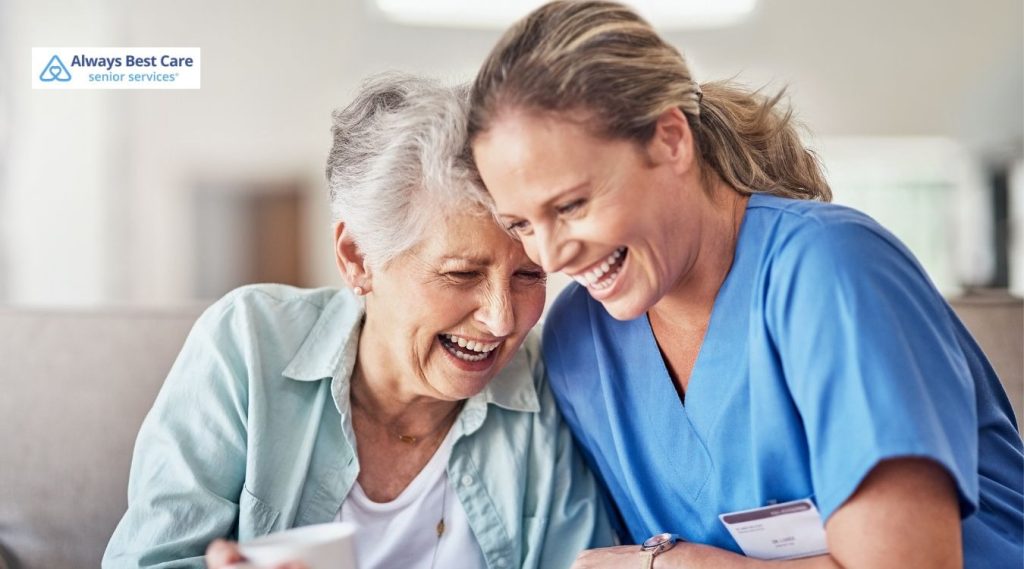 Caring nurse sitting close with senior woman on couch, sharing a warm conversation, Always Best Care senior services logo in corner.