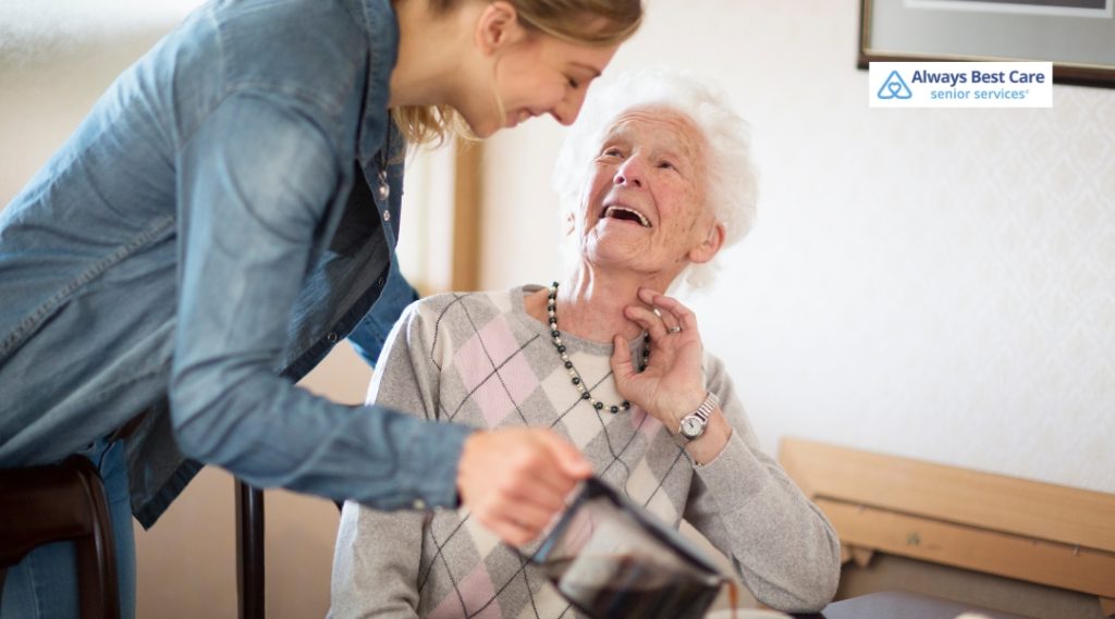 A caregiver is helping an elderly woman with some sort of activity, with the elderly woman smiling joyfully, creating a nurturing and positive environment.