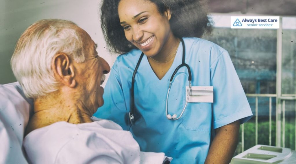 Caregiver in blue smiling with a senior man who is in bed
