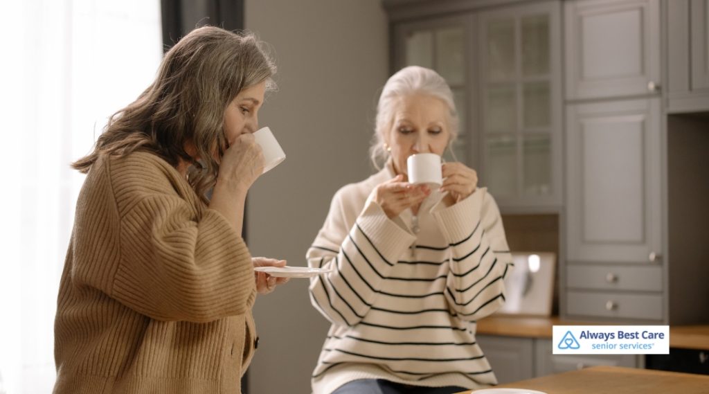 Two senior women enjoying cups of tea or coffee together in a cozy, bright kitchen.