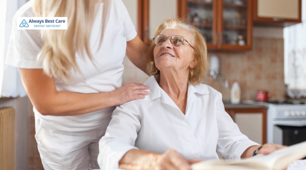 A caregiver smiling at a senior woman as they share a moment of connection in a kitchen setting.