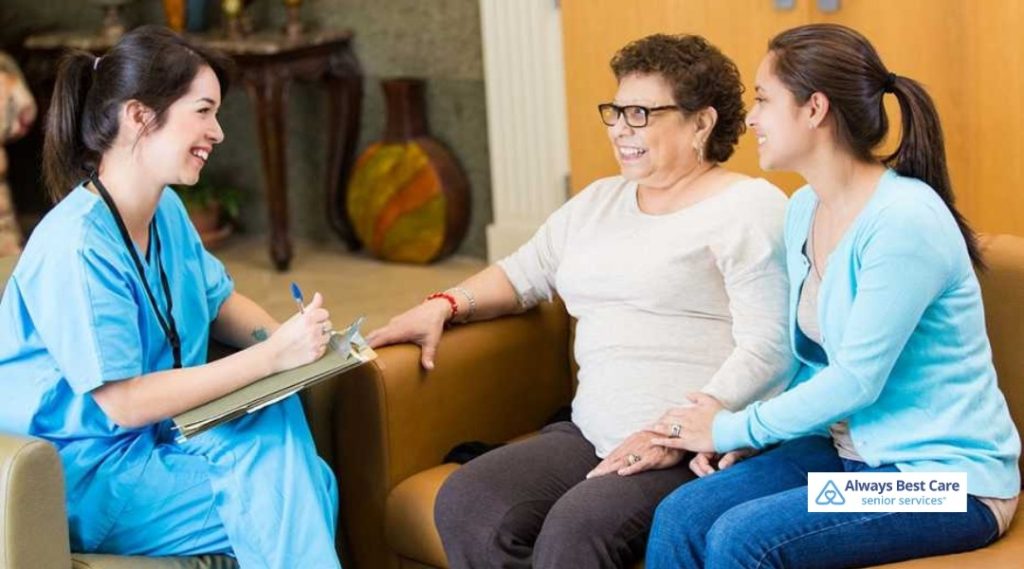 Nurse speaking with an older woman and her daughter during an in-home care consultation, reviewing notes and discussing care needs.