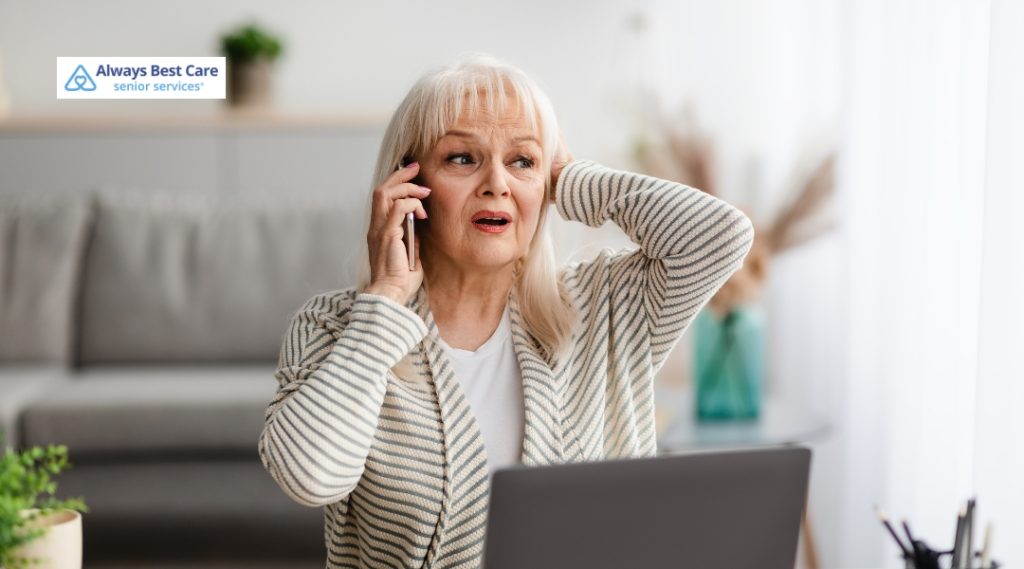 Stressed older woman talking on the phone in front of a laptop, reacting to a possible fraud attempt.
