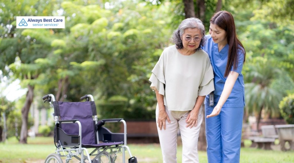 Caregiver helping a senior woman stand safely in a living room.