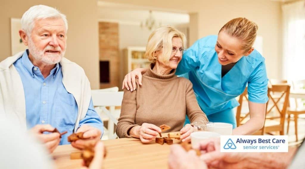 Caregiver engaging seniors in a table activity at home, encouraging social connection and independent living.