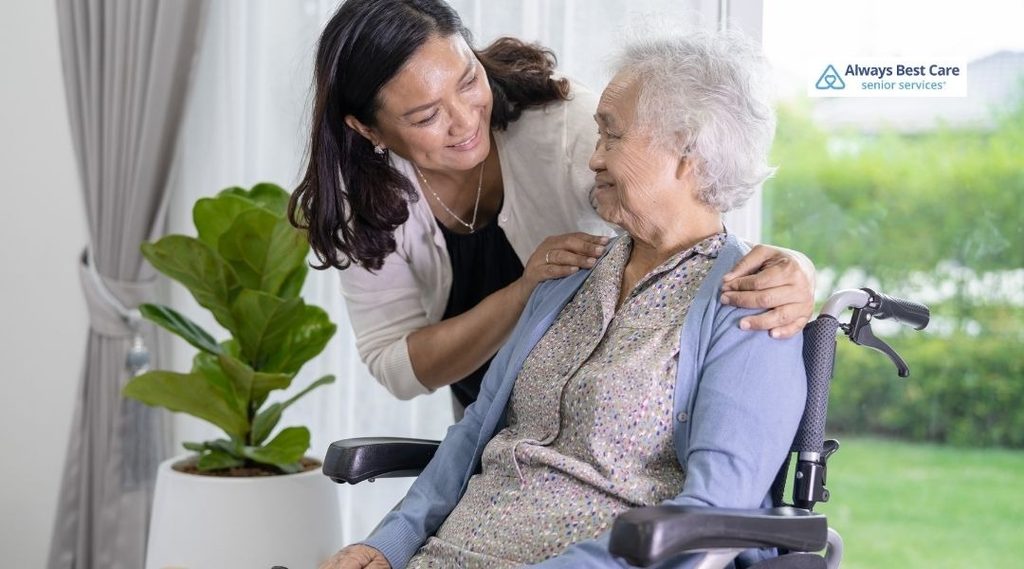Companion caregiver offering reassuring support to an older woman seated in a wheelchair at home.