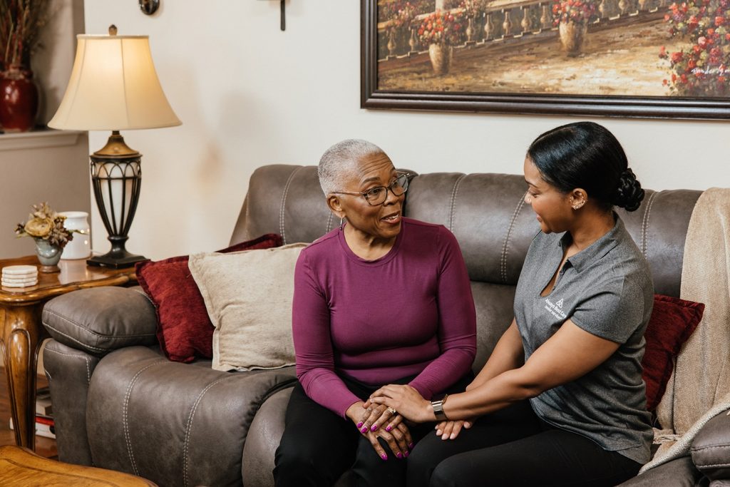 Companion caregiver offering reassuring support to an older woman seated in a wheelchair at home.