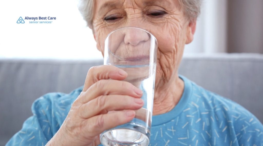 Older woman sitting on a bed and taking medication with water.
