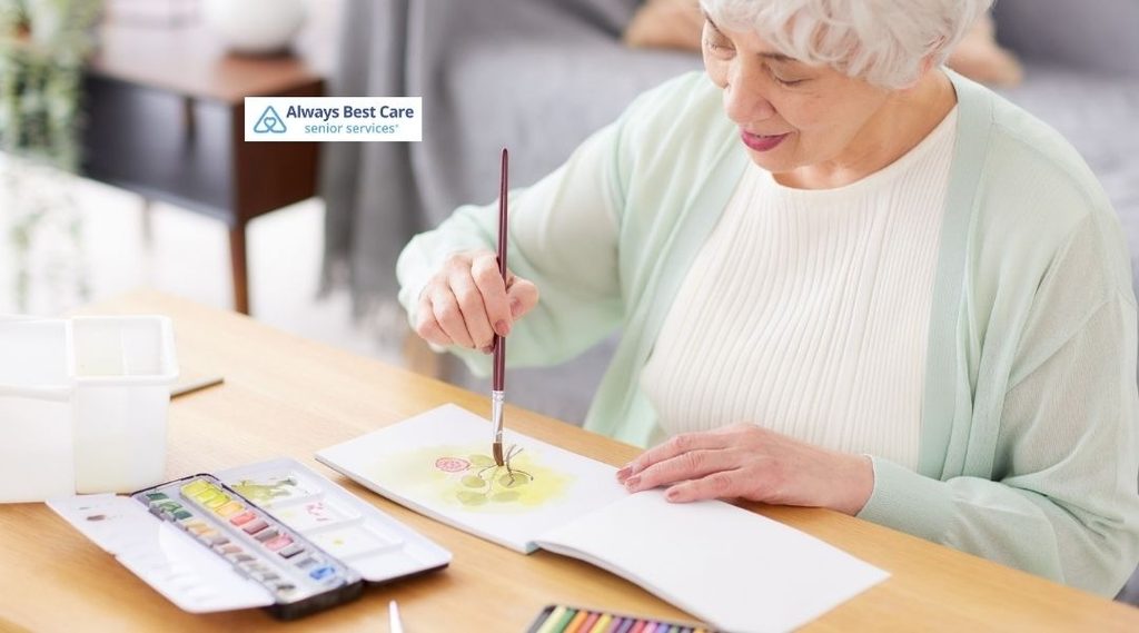 Older woman painting with watercolours at a table during a creative activity at home.