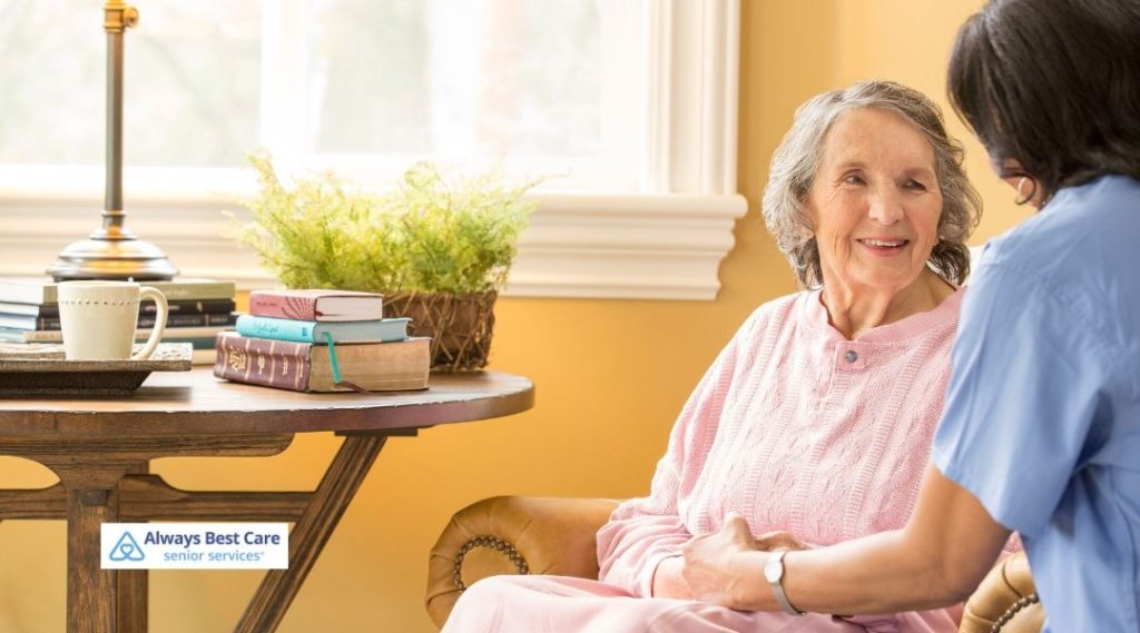 Caregiver sitting with an older woman in her living room, offering companionship and emotional support at home.