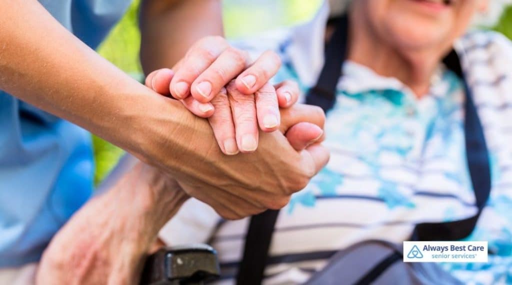 Caregiver holding hands with a senior individual in a wheelchair, offering gentle support and ensuring comfort.