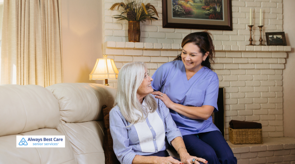 Caregiver sitting beside a senior woman on a couch, offering comfort and friendly conversation at home.