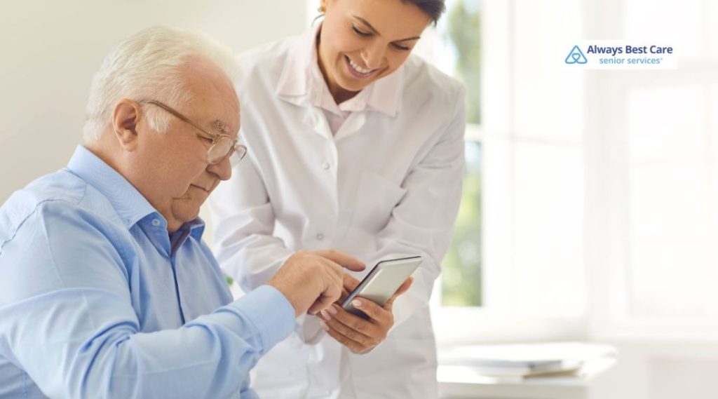 Caregiver showing an elderly man how to use a smartphone during a home care visit.