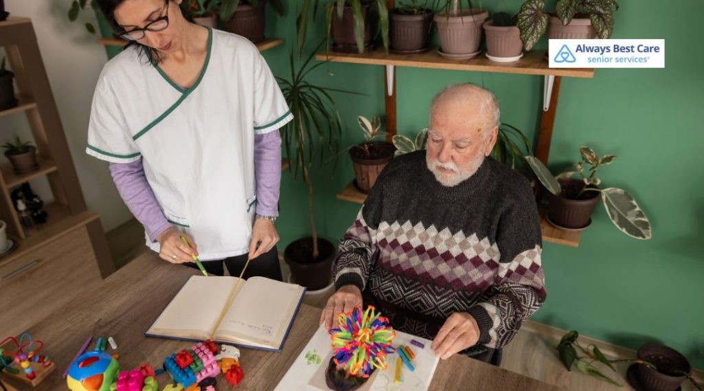 Caregiver guiding an elderly man through a cognitive stimulation activity using educational tools in a home care environment.