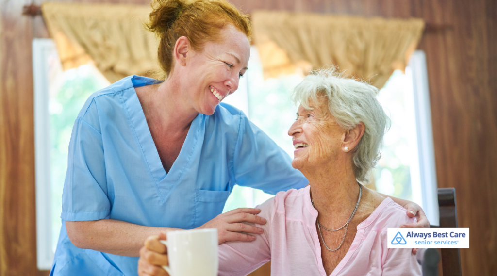 A caregiver and senior woman sharing a joyful moment over a cup of tea, in a warm and inviting home environment. Always Best Care senior services logo visible at the bottom.