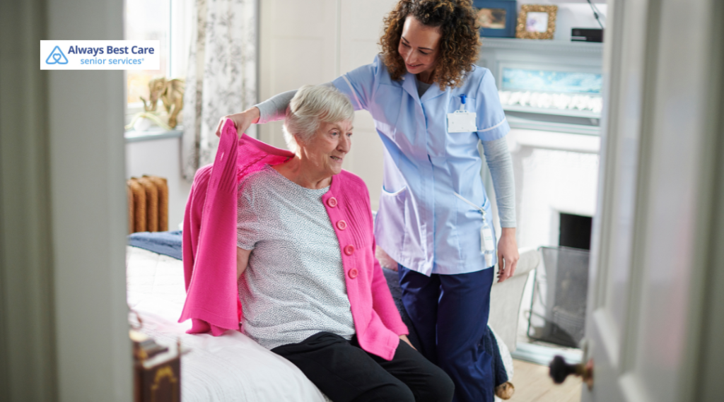 A caregiver assisting a senior woman in getting dressed, helping her put on a cardigan with a caring touch.