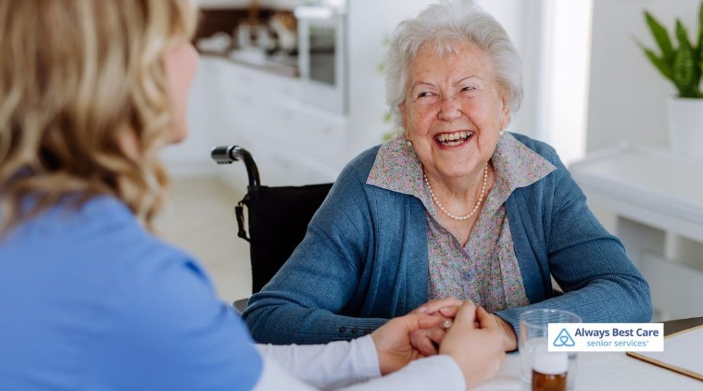 A caregiver helps an elderly woman stand, offering support and care. They both smile at each other, enjoying their time together, with a cozy and peaceful home environment in the background.