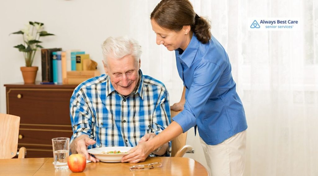 A caregiver serves a meal to a senior man at a table