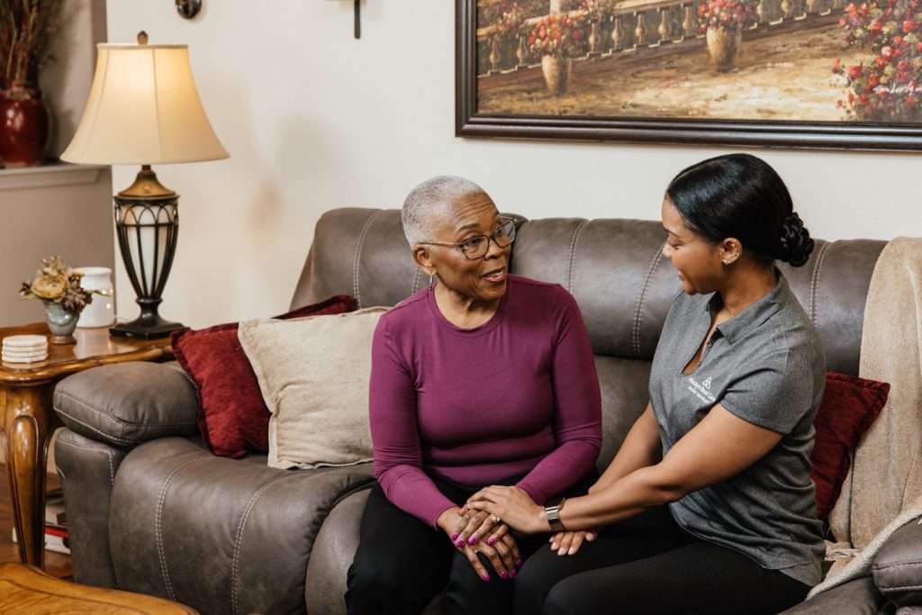 Two women sit on a couch and talk warmly in a comfortable living room.