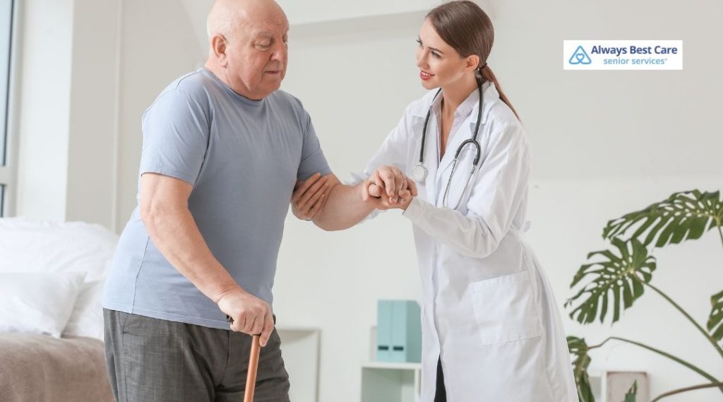 Caregiver supporting an elderly man with balance and mobility exercises at home