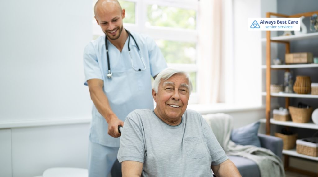 A caregiver gently pushes a senior man’s wheelchair, helping him move around in a well-lit, comfortable home environment. The elderly man smiles warmly, appreciating the support.