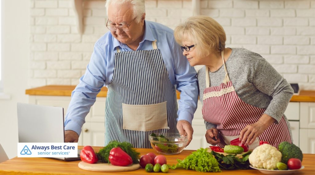  A senior couple cooking together in a kitchen with a laptop
