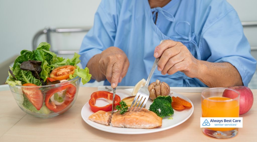 A senior man in a hospital gown enjoys a nutritious meal with salmon, vegetables, and juice, emphasizing balanced senior diets.