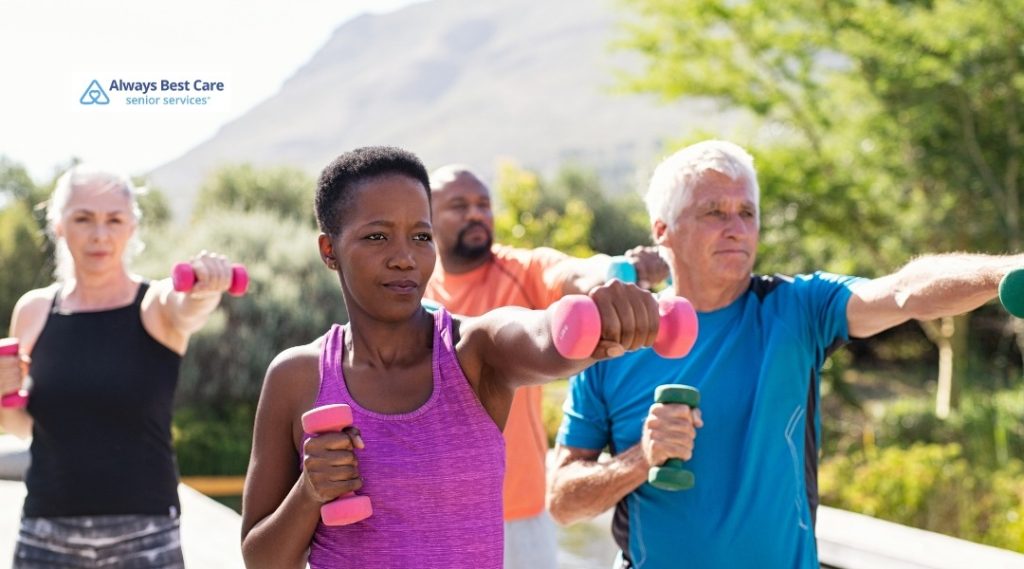 8. Group of active seniors walking together on a sunny park trail, wearing casual fitness clothing, with the Always Best Care Senior Services logo in the corner.
