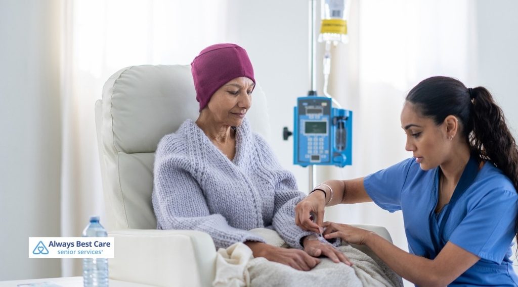 Healthcare professional tending to an IV line on a seated woman’s hand beside an infusion pump