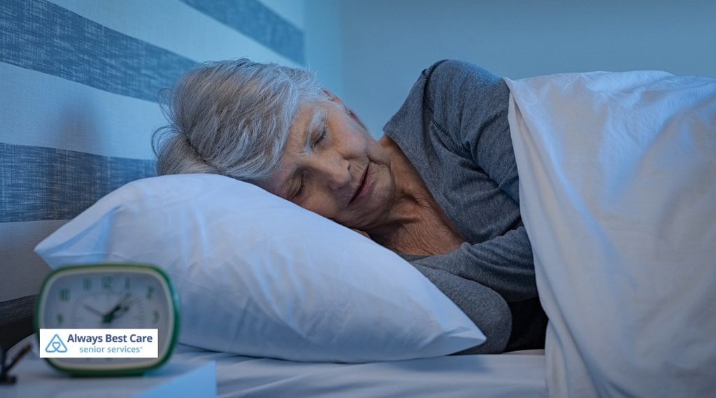 Senior woman sleeping on her side with an alarm clock on the bedside table.